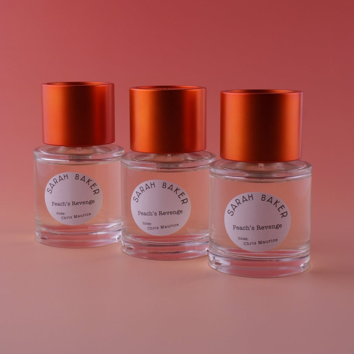 Three Sarah Baker Peach's Revenge bottles on a peach backdrop