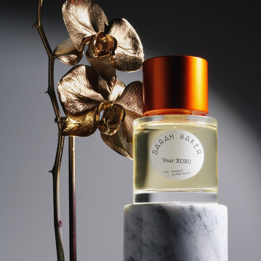 Sarah Baker Year XOXO beside a gilded orchid on a marble plinth