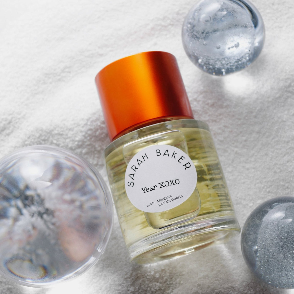 Sarah Baker Year XOXO resting in white sand with glass spheres